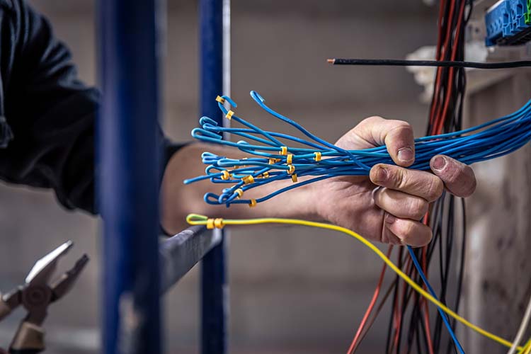 A hand holding a bundle of blue and yellow wires, with pliers and a steel frame behind