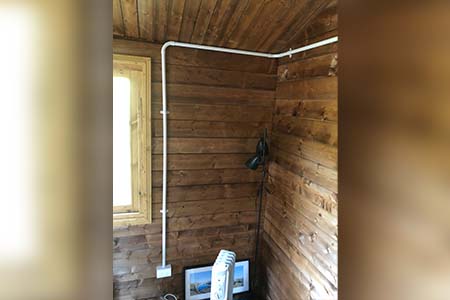 Inside a timber-lined room, white conduit run along the wall and a small heater on the floor