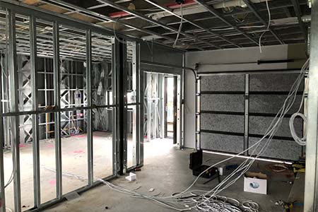 Inside a steel-stud framed building, cables hanging from the ceiling and walls, red layout marks on the slab