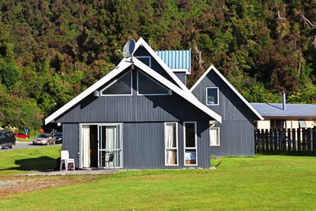 A dark grey gabled house with white trim, a green lawn and bush behind
