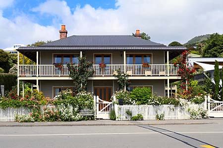A two-storey villa with a balcony, rose garden and picket fence, seen from the street