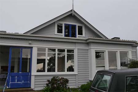 A grey weatherboard villa with a blue door and a car at the right