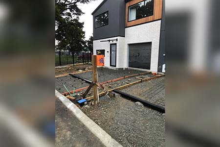 A modern dark, white and timber-clad house with conduit and formwork in the gravel driveway