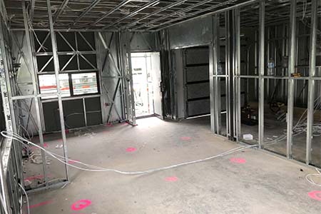Inside steel-stud framing, cables on the slab, pink marks and window and door openings